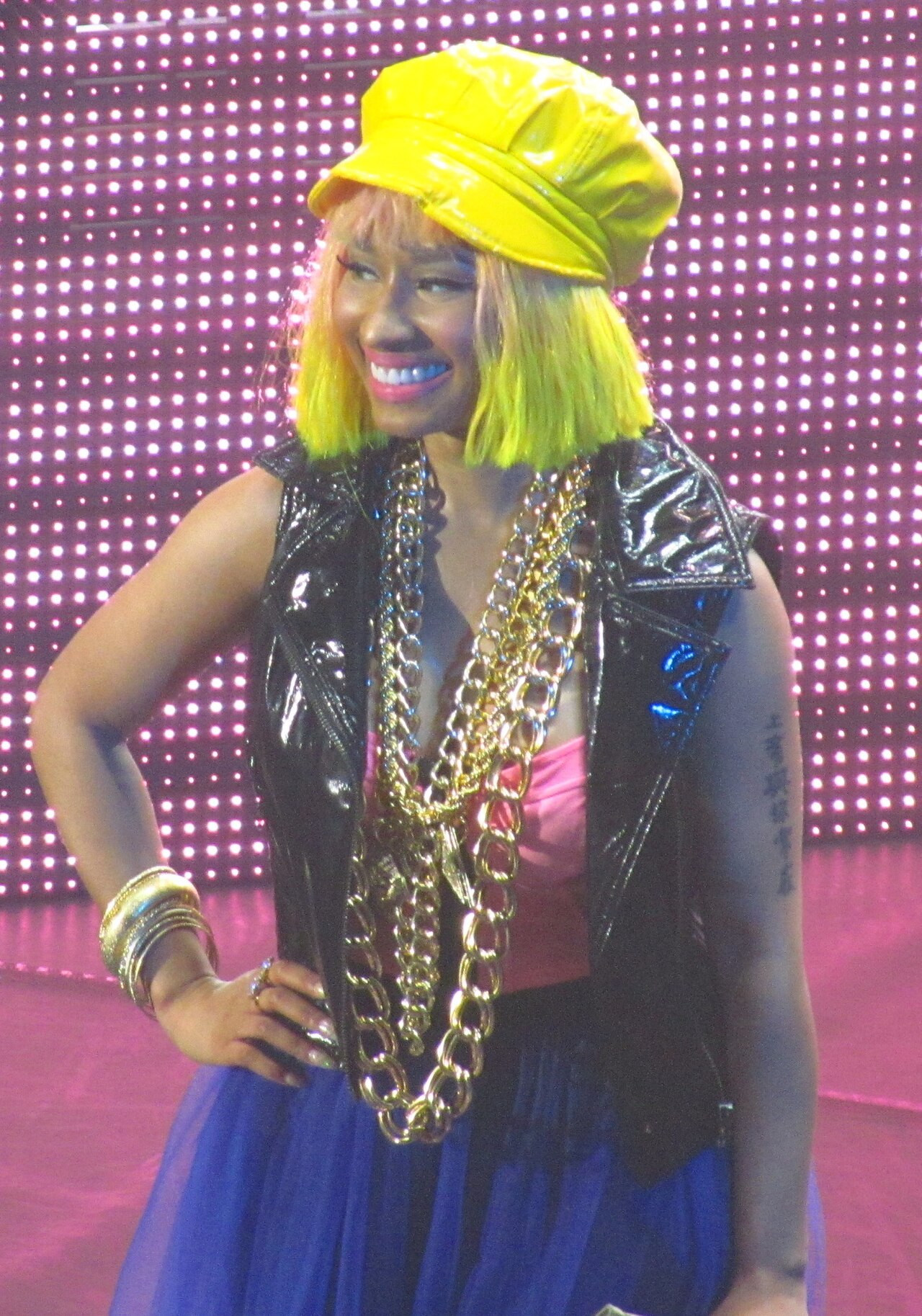 Nicki Minaj con berretto giallo, capelli verdi neon, catene d'oro e tutù blu