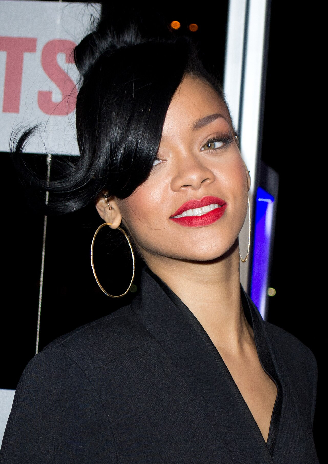 Rihanna im schwarzen Blazer mit Creolen, rotem Lippenstift und dunklem Steckhaar