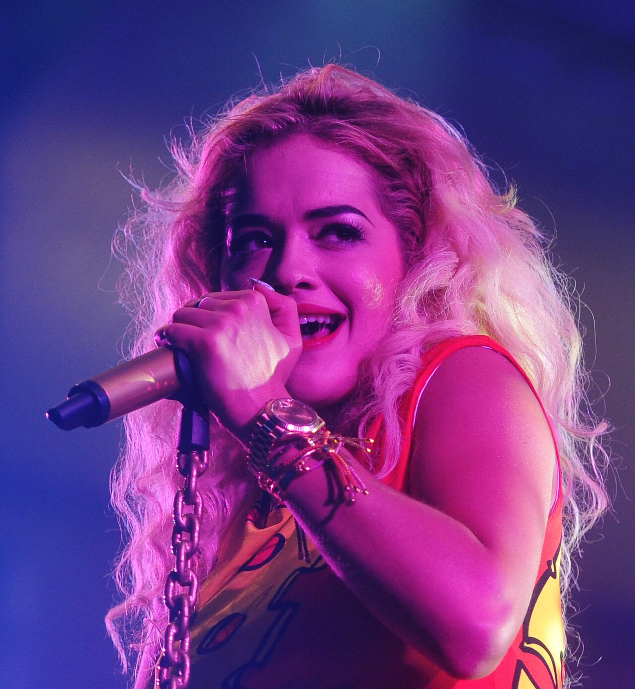 Rita Ora mặc váy vàng rực với tóc xoăn vàng dưới ánh đèn sân khấu màu hồng